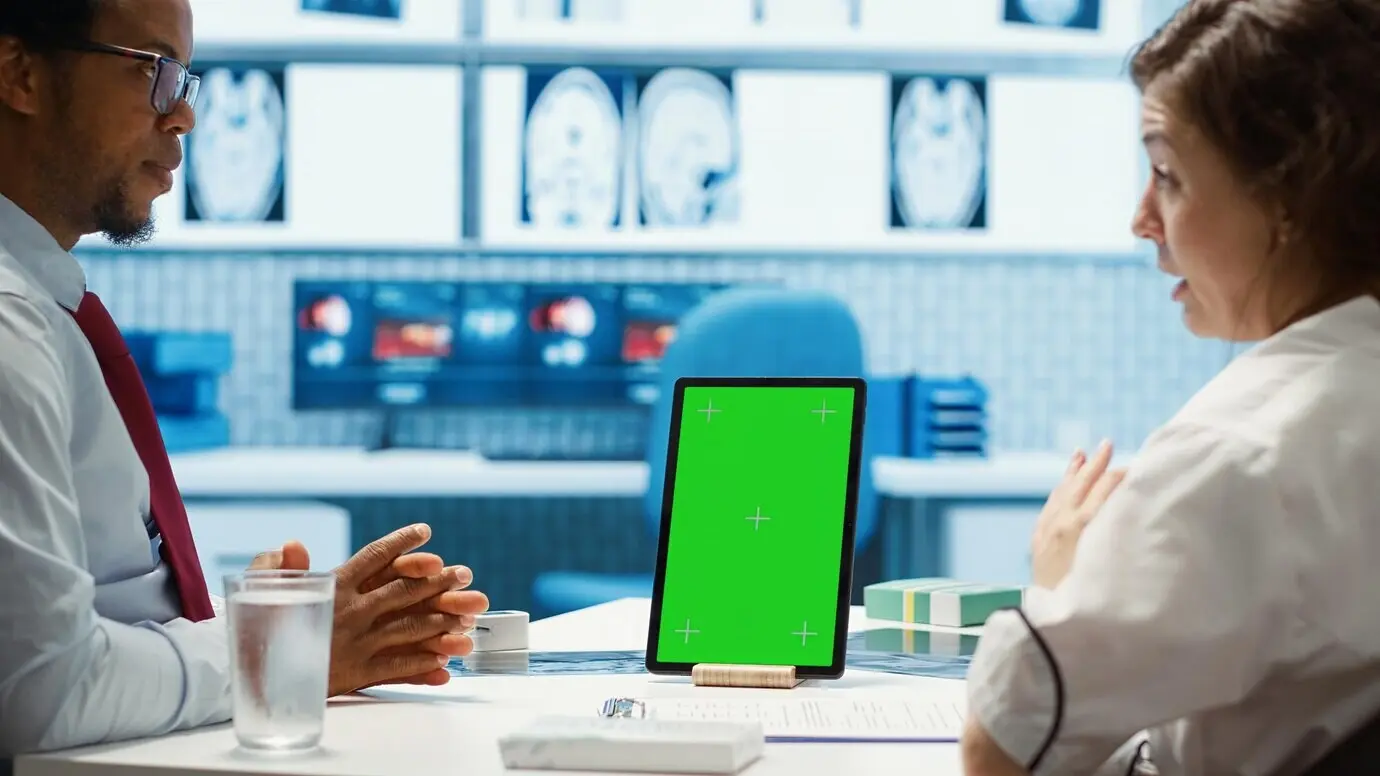 Врач общей практики указывает на макет с зелёным экраном на устройстве.